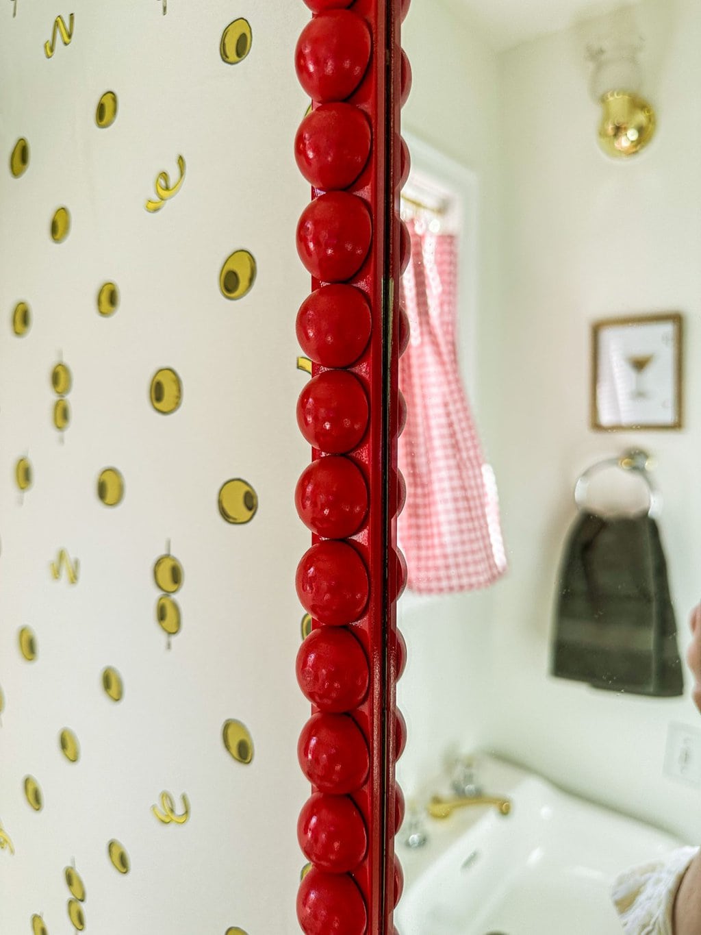 border edge of the bobbin mirror with red spray paint on top of olive and lemon white wallpaper 