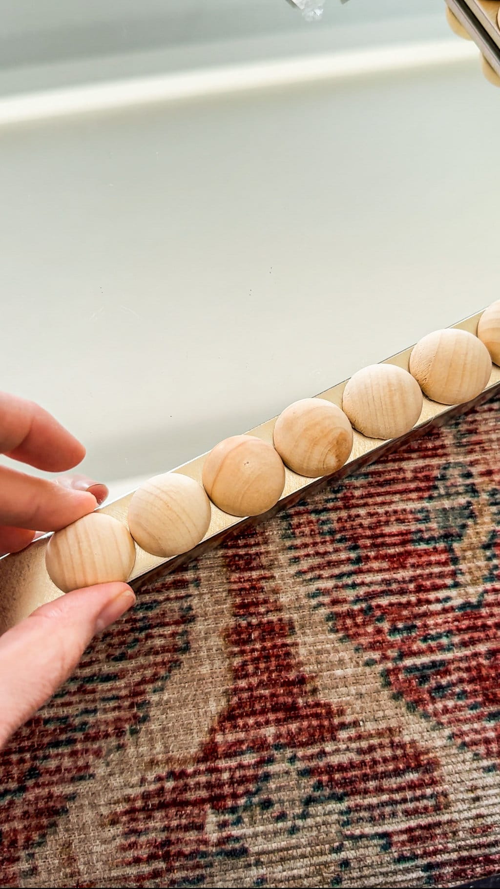 a half wooden sphere being placed onto a mirrors  borders edge with other half wooden spheres glued on