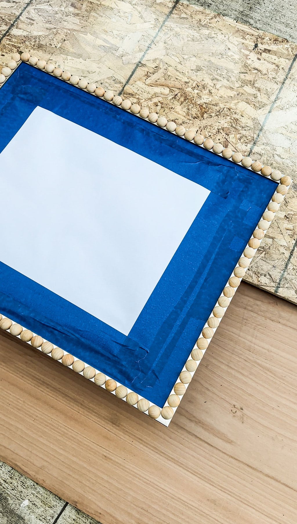 a mirror that has many half wooden spheres glued on the border and has been lined with blue masking tape and paper 