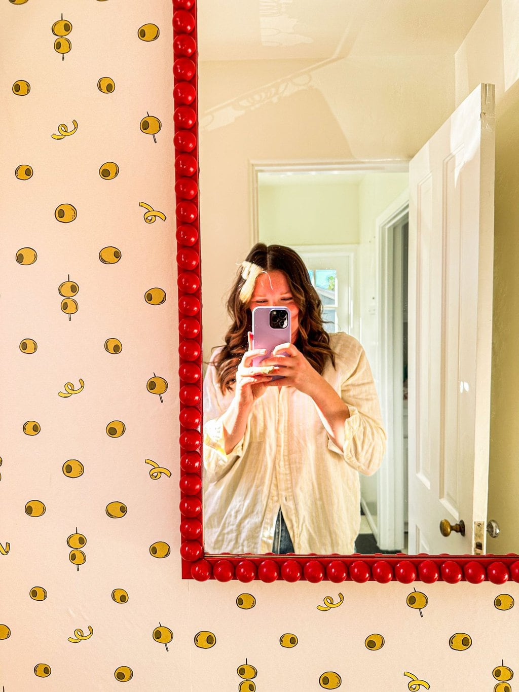 Elizabeth taking a selfie in a red diy french bobbin mirror with olive wallpaper seen on the left side