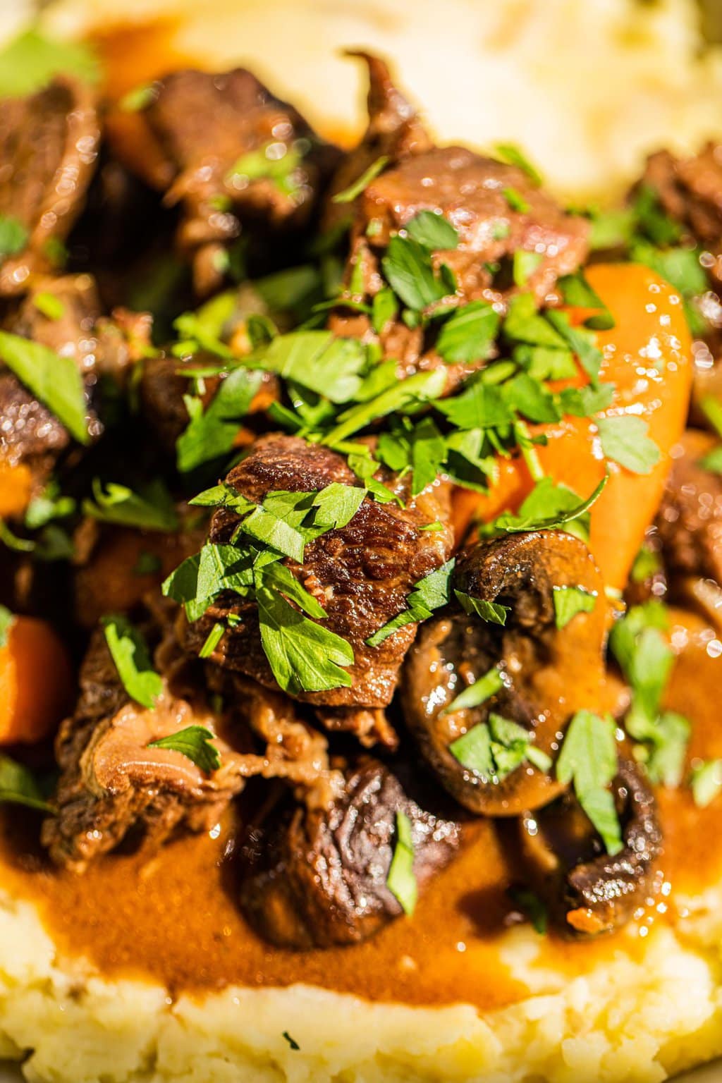 close up photo of the stewed beef garnished in fresh parsley and served atop mashed potatoes