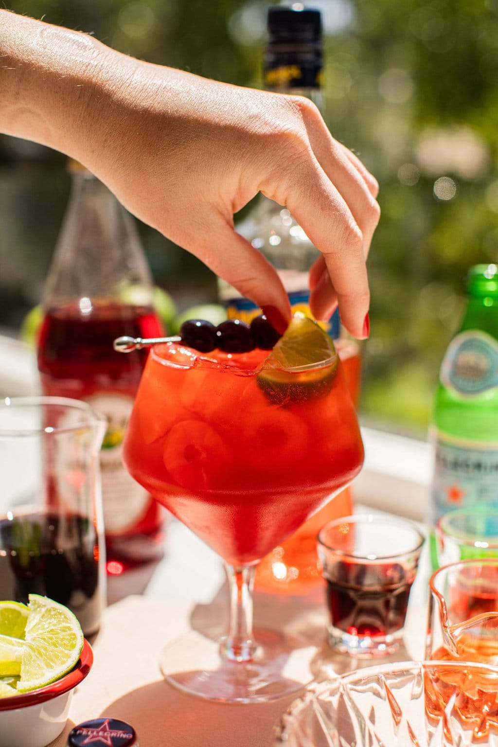 garnishing a glass of cherry spritz with a lime wedge