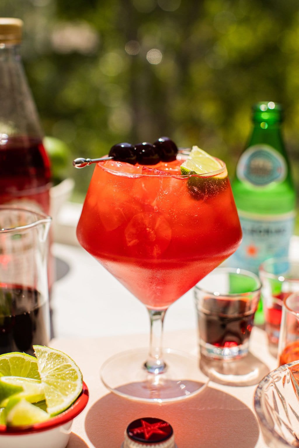 a glass full of a cherry spritz garnished with cherries and a lime wedge