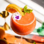 a frozen strawberry aperol spritz garnished with a slice of orange and a flower
