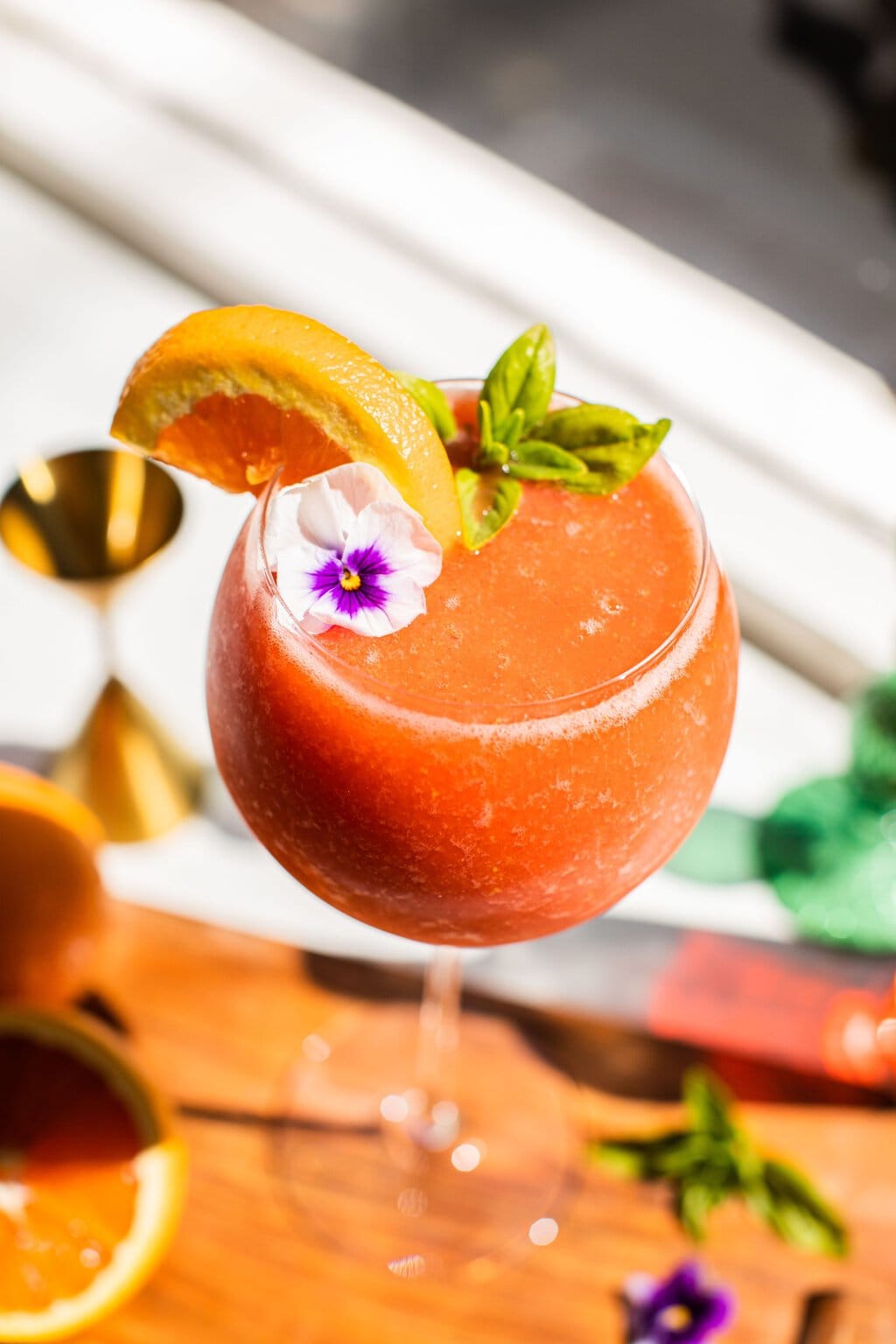 a frozen strawberry aperol spritz garnished with a slice of orange and a flower