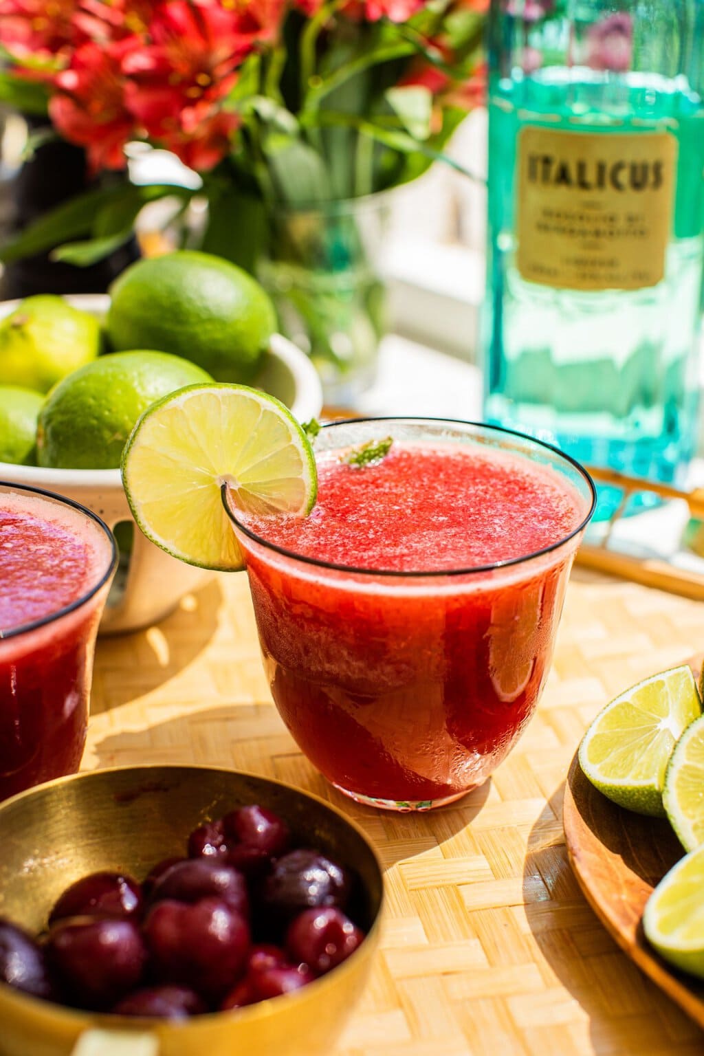 cherry margarita garnished with lime, with a bottle of italicus in the background and a bowl of cherries in the foreground