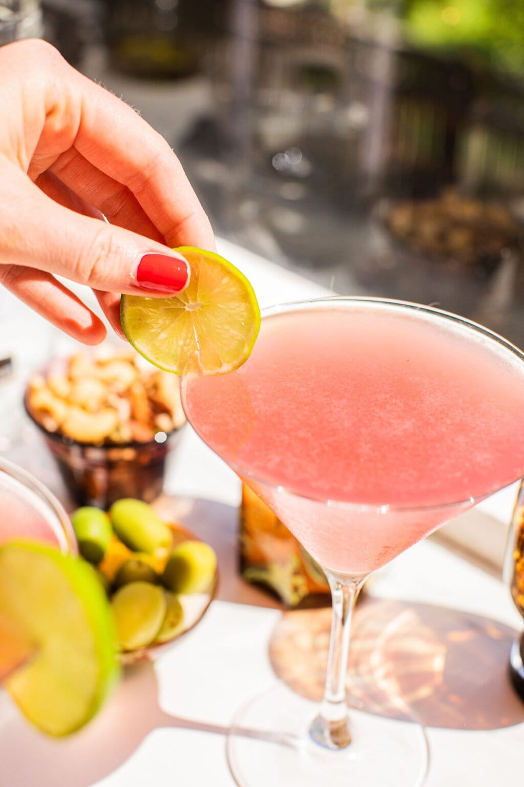 elizabeth adding a lime wheel as garnish to the pink cosmo in a martini glass