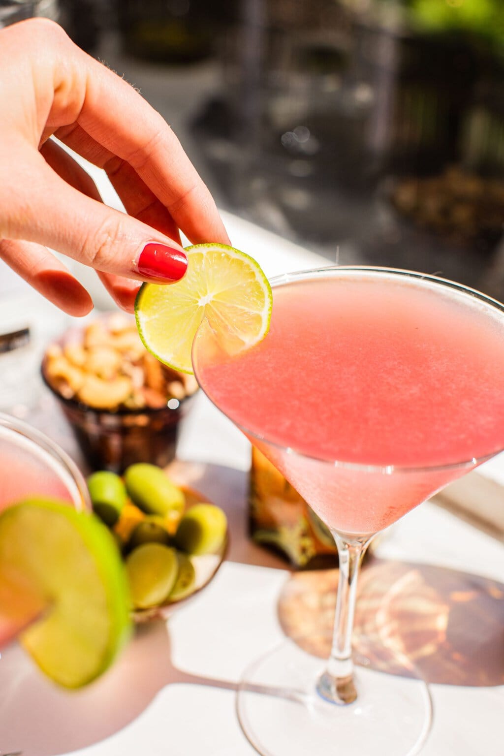 elizabeth adding a lime wheel garnish to the light pink cosmo