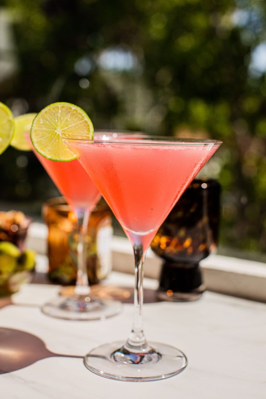 a pink cosmo in a martini glass garnished with a lime wheel