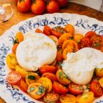 a white and blue bowl full of marinated tomatoes and two balls of burrata