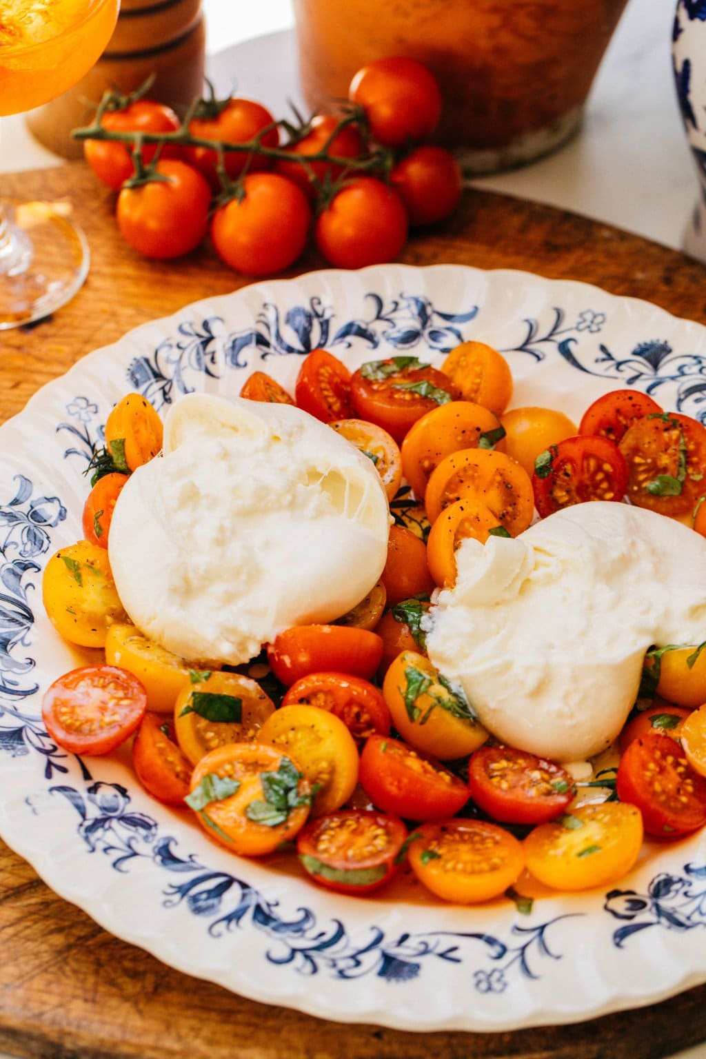 a white and blue bowl full of marinated tomatoes and two balls of burrata