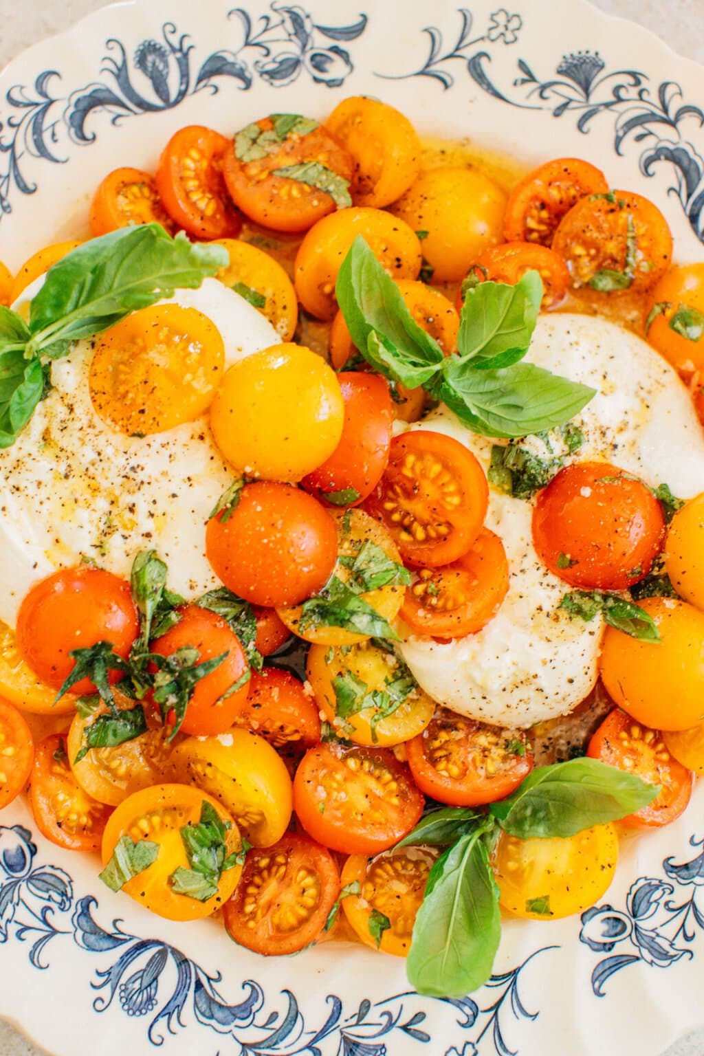 a close up shot on a bowl full of dressed tomatoes, creamy burrata, and fresh basil