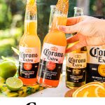 a hand holding a bottle of corona garnished with a lime wedge and rimmed with tajin next to another bottle