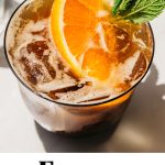 a glass of an espresso spritz with an orange slice and mint leaf garnish and text overlay