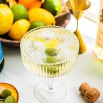 a spritz with olives and lemon inside it and a bowl of oranges, limes, and lemon in the background