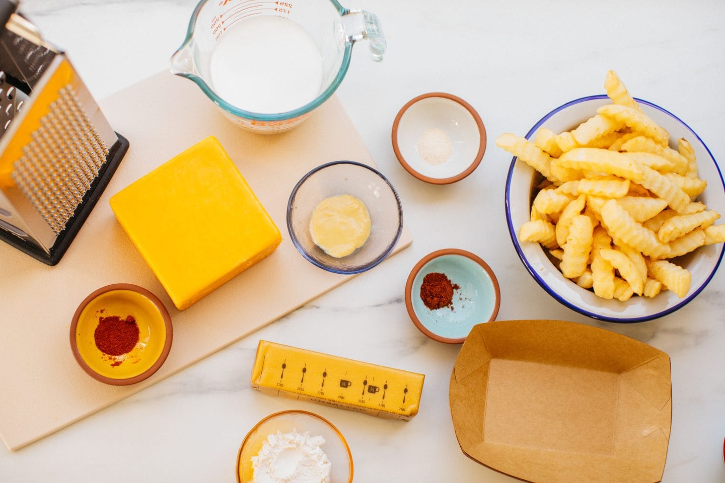 a bowl of air fryer french fries, seasonings, milk, cheddar, and butter