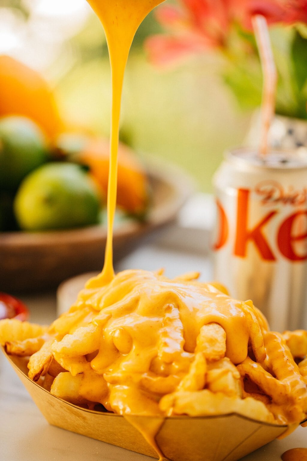 fries with cheese being poured over them and a diet coke out of focus in the background