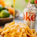 french fries with cheese sauce drizzling on top of them and a diet coke in the background