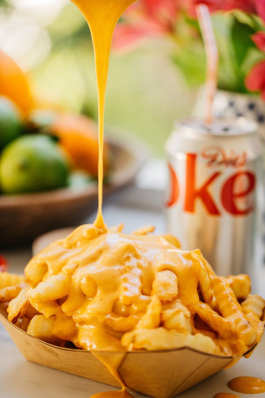 french fries with cheese sauce drizzling on top of them and a diet coke in the background