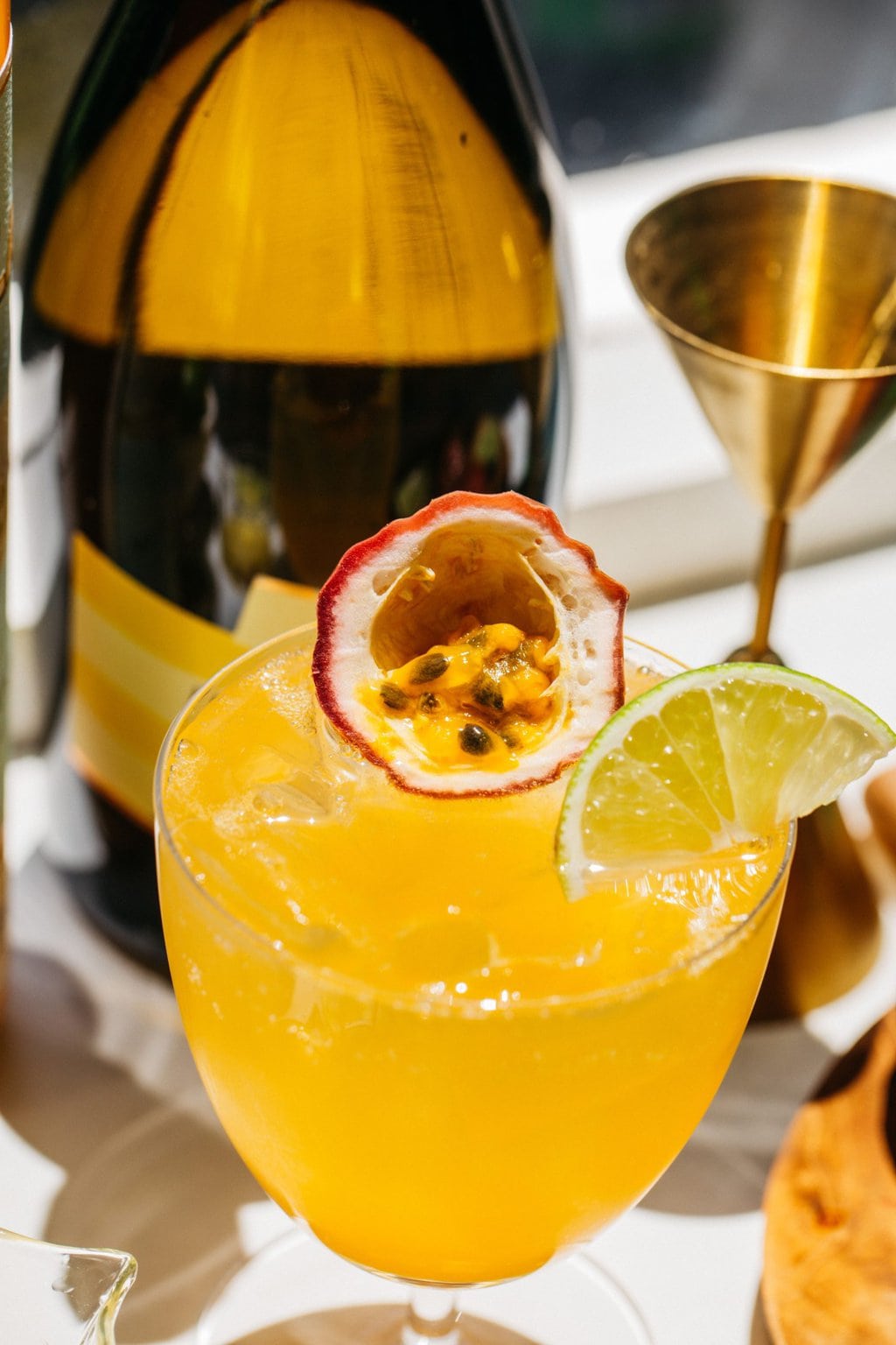 a close up of a passion fruit spritz in a wine glass garnished with a slice of fruit and a lime wedge