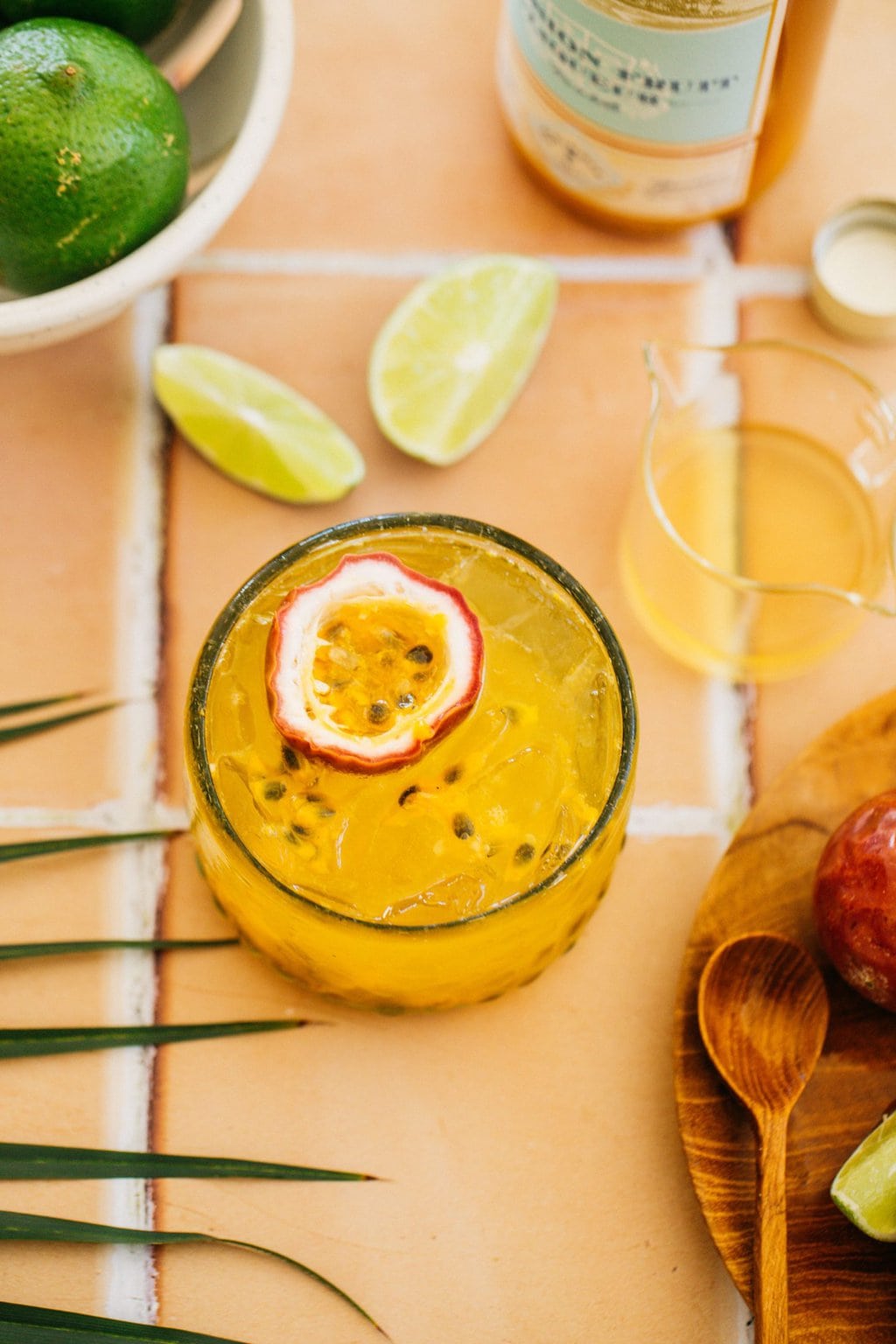 a spritz with passion fruit garnish on peach tile with lime wedges around it 