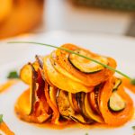 a serving of ratatouille vegetables on a white plate with the sauce drizzled in a circle around it