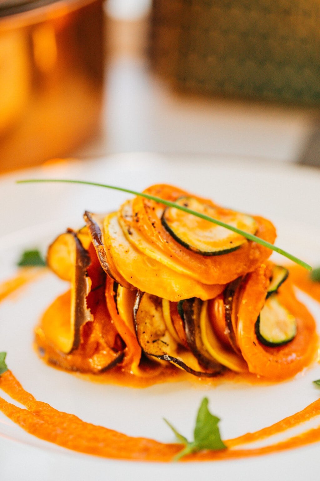 a serving of ratatouille vegetables on a white plate with the sauce drizzled in a circle around it