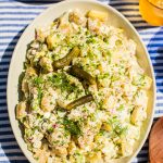 a large cream serving bowl filled with potato salad garnished with fresh dill and dill pickles