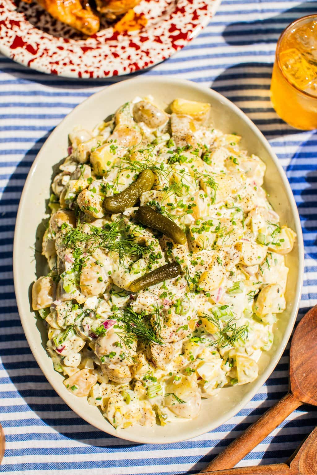 a large cream serving bowl filled with potato salad garnished with fresh dill and dill pickles