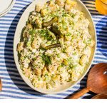 a bowl of dill potato salad in a large white serving bowl on a blue and white striped table cloth