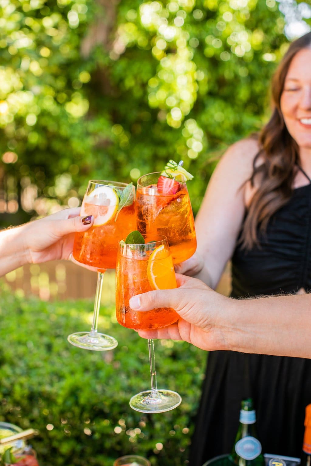 three people clinking their aperol spritz glasses together