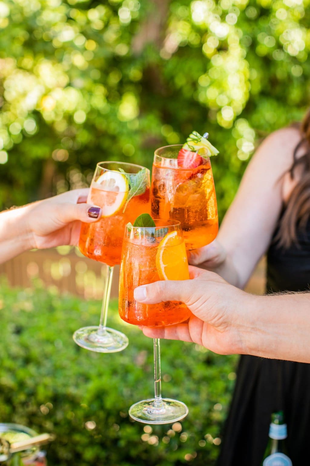 three people clinking glasses of aperol spritz together