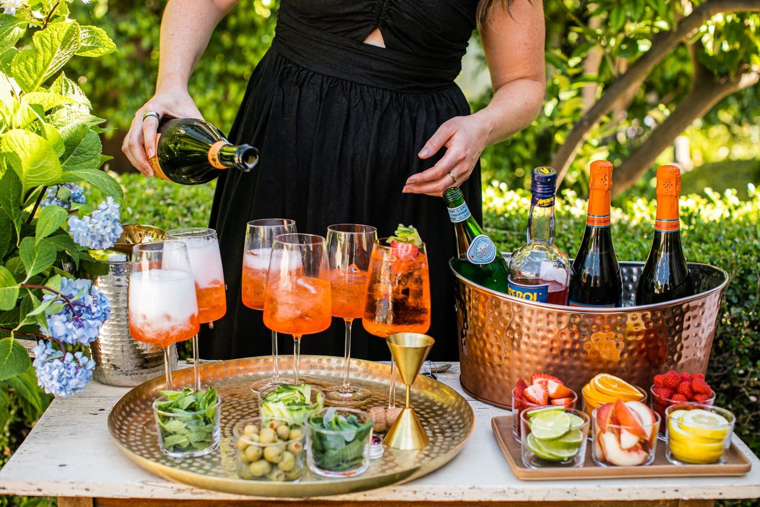 elizabeth pouring aperol spritz' with with garnishes in individual glasses in front