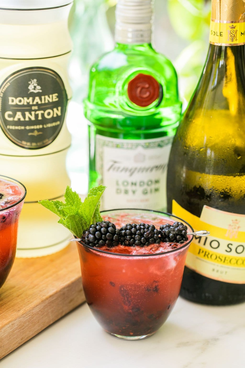 a blackberry gin spritz surrounding by bottles of prosecco, gin, and ginger liqueur 