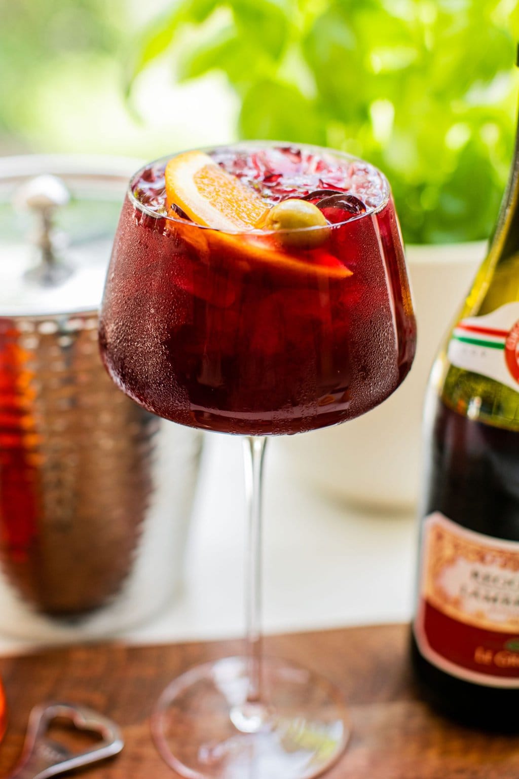 a glass of lambrusco spritz garnished with an olive and orange slice with condensation on the outside