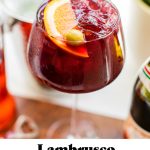 a lambrusco pomegranate spritz with an orange garnish and text overlay at the bottom of the image