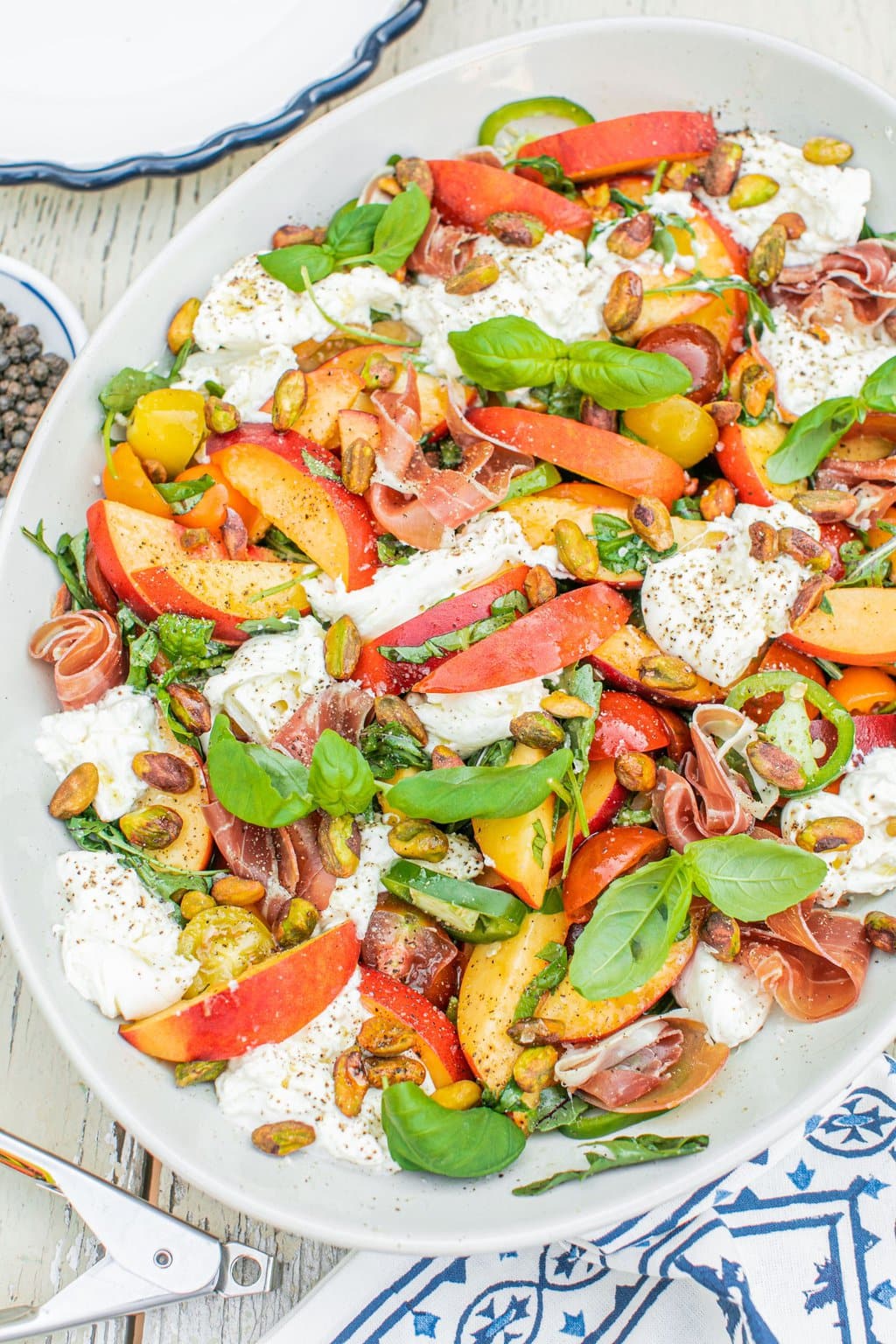 a large serving bowl full of peach burrata salad with proscuitto, tomatoes, and vinaigrette