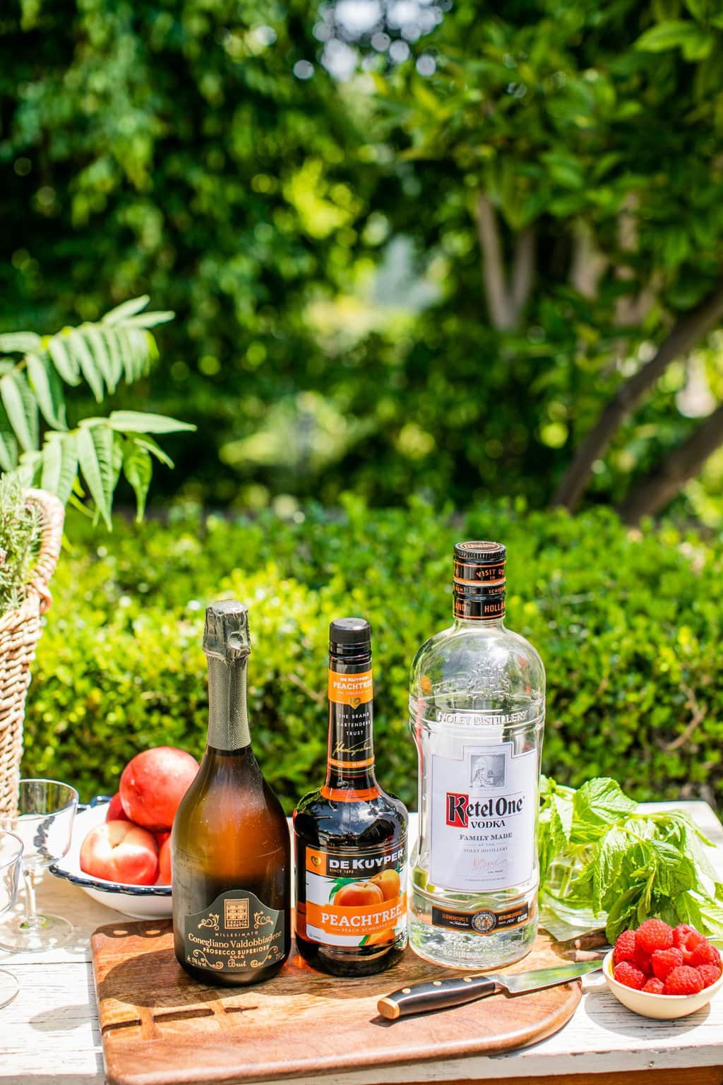 ketel one, peach schnapps, prosecco, peaches, mint, and raspberries on a chopping board and outdoor table