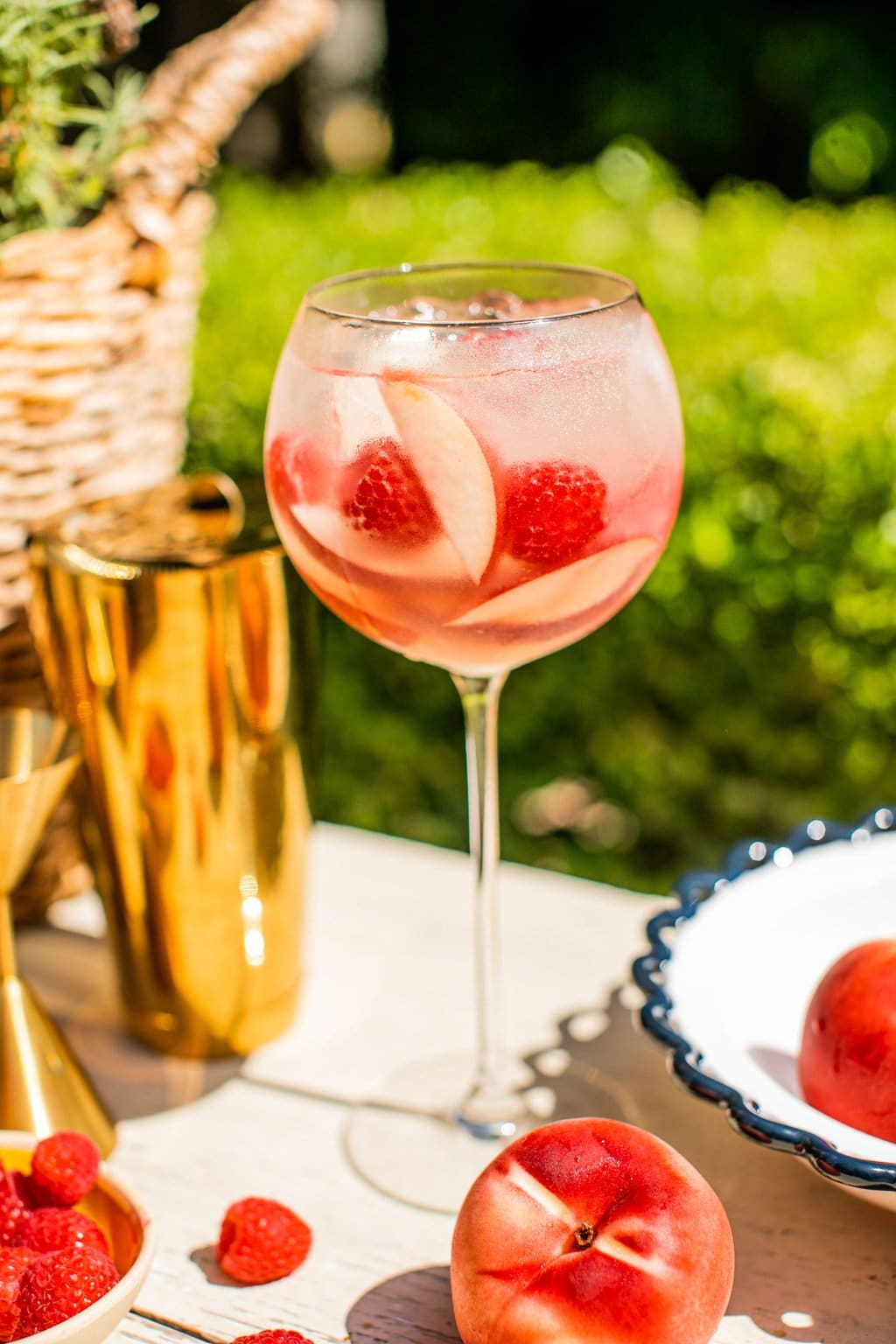 a peach spritz beside a golden cocktail shaker and raspberries for garnish