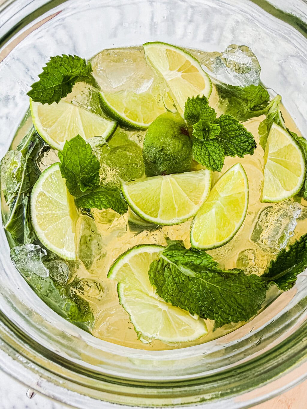 a top down view of a hugo spritz with fresh limes, mint leaves and ice