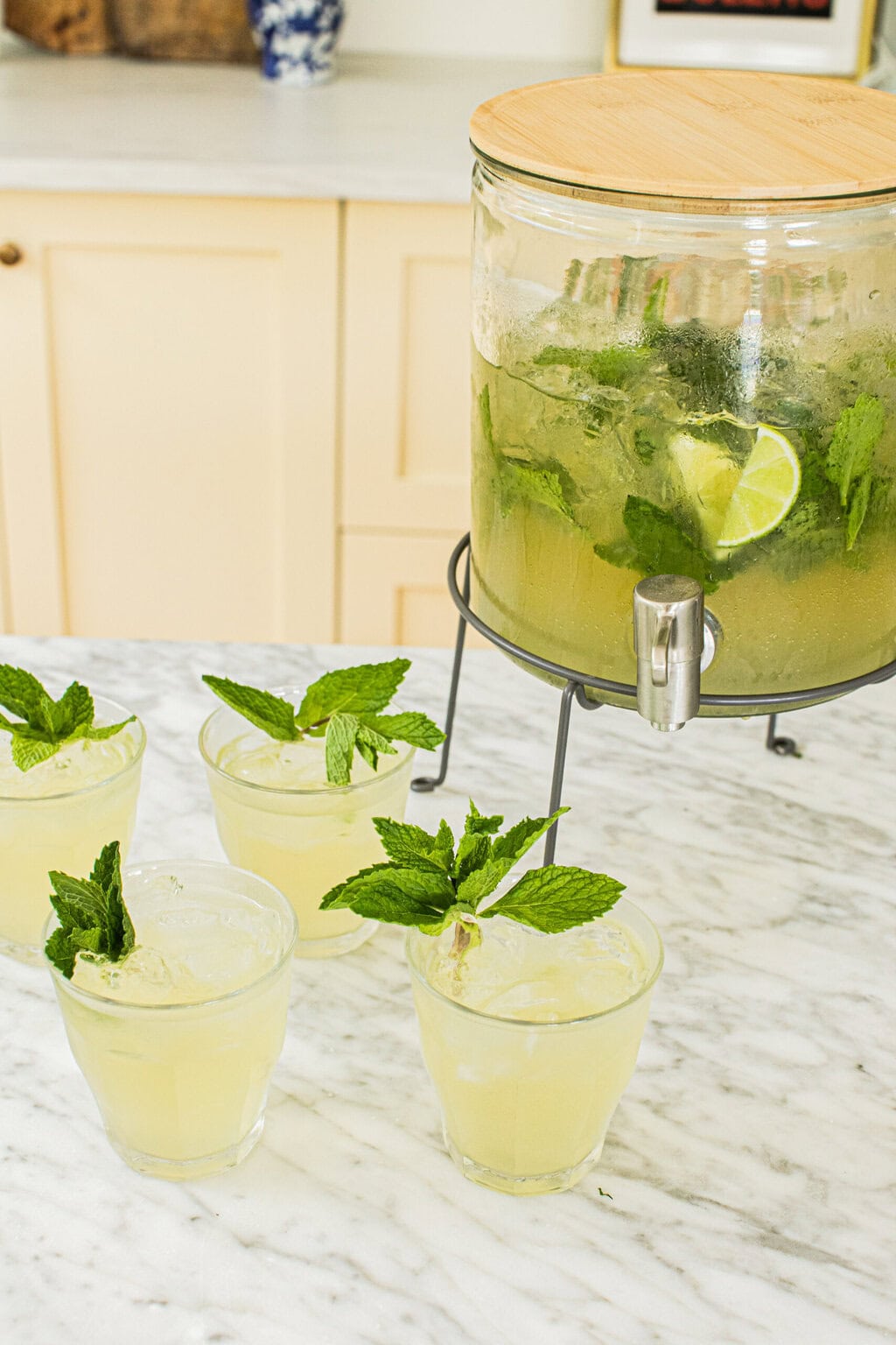 four low glasses filled with hugo spritz and garnished with fresh mint sprits, a drink dispenser half full with hugo spritz
