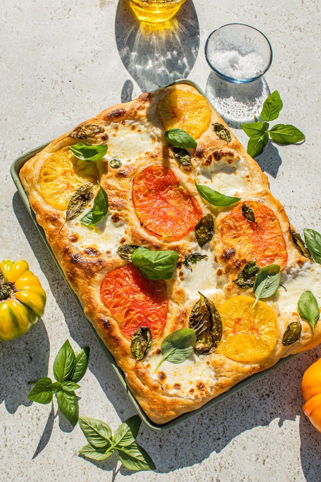 a baking dish full of caprese focaccia bread topped with tomato and mozarella slices, as well as basil leaves