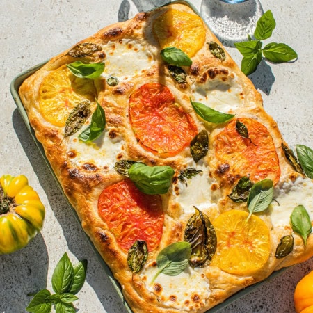 a baking dish full of caprese focaccia bread topped with tomato and mozarella slices, as well as basil leaves