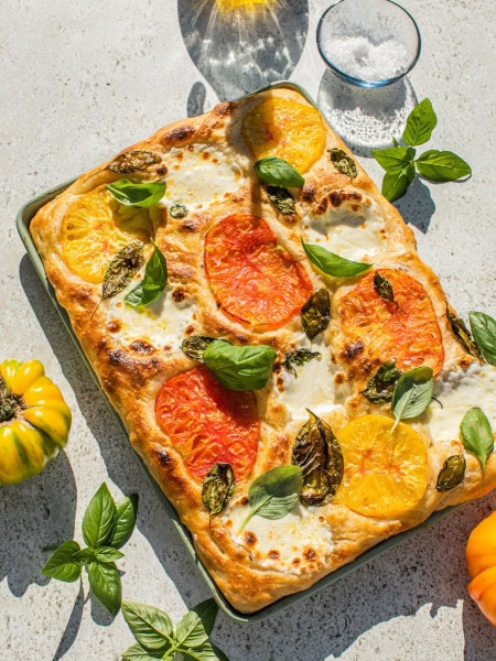 a baking dish full of caprese focaccia bread topped with tomato and mozarella slices, as well as basil leaves