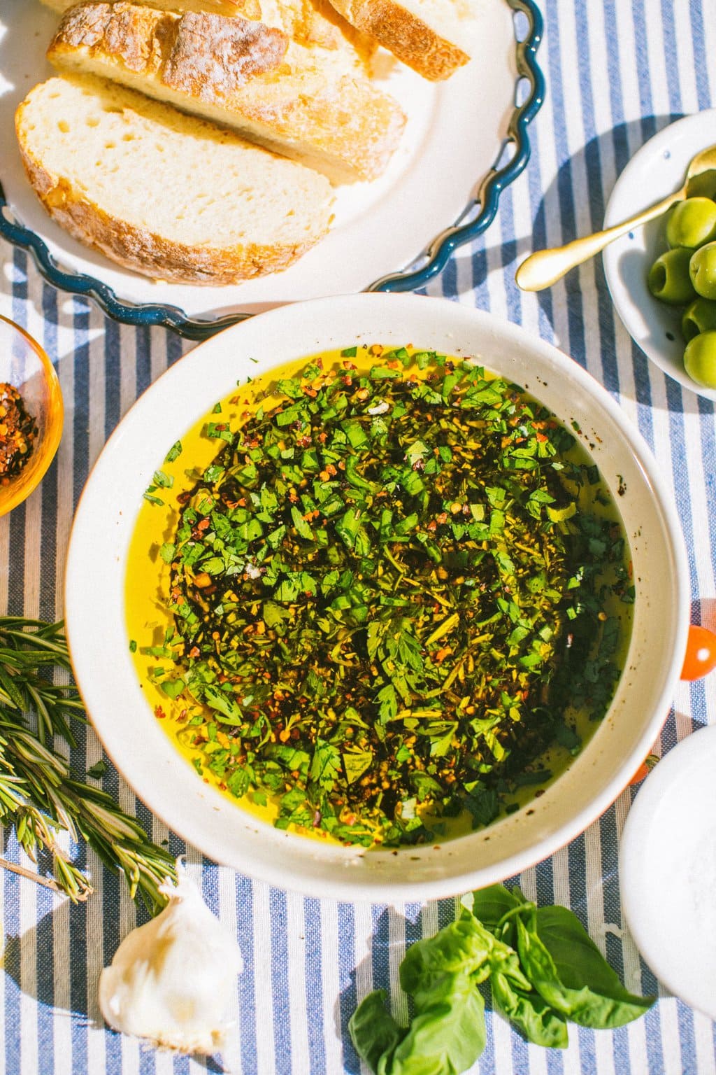 a large bowl of the balsamic and oil bread dip on a white and blue striped table cloth with various bowls and ingredients partially out of the picture around it 