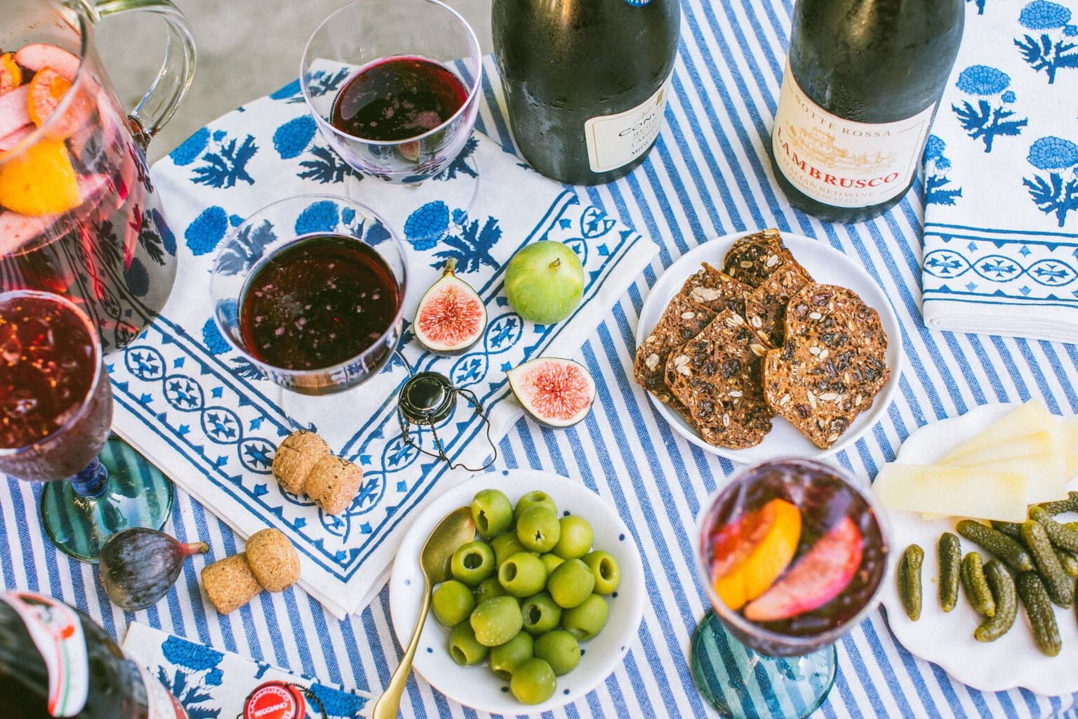 olives, bread, pickles, and glasses of lambrusco on a blue and white striped table cloth