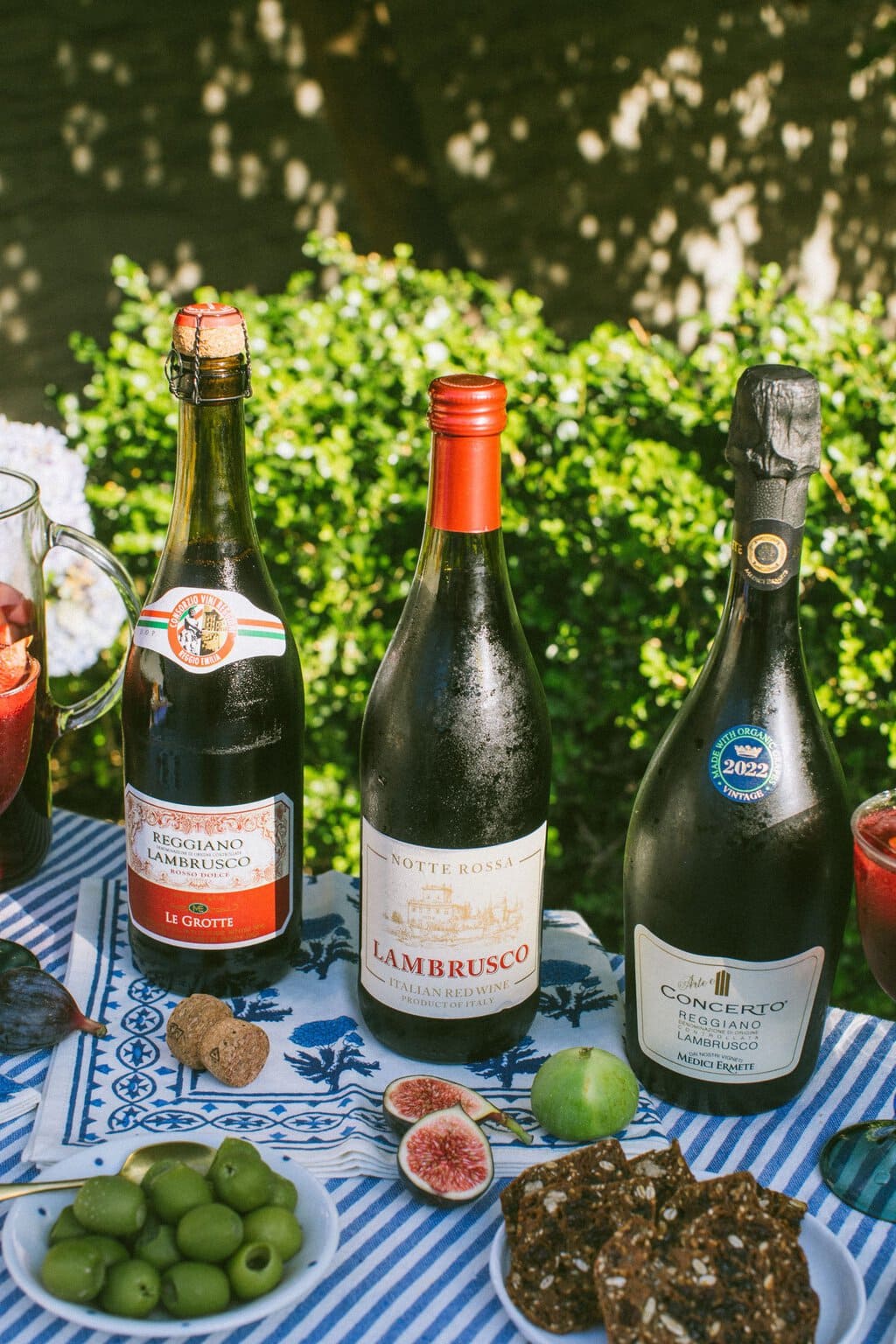 three different bottles of lambrusco with figs, olives, and other fruits in front of them on the table