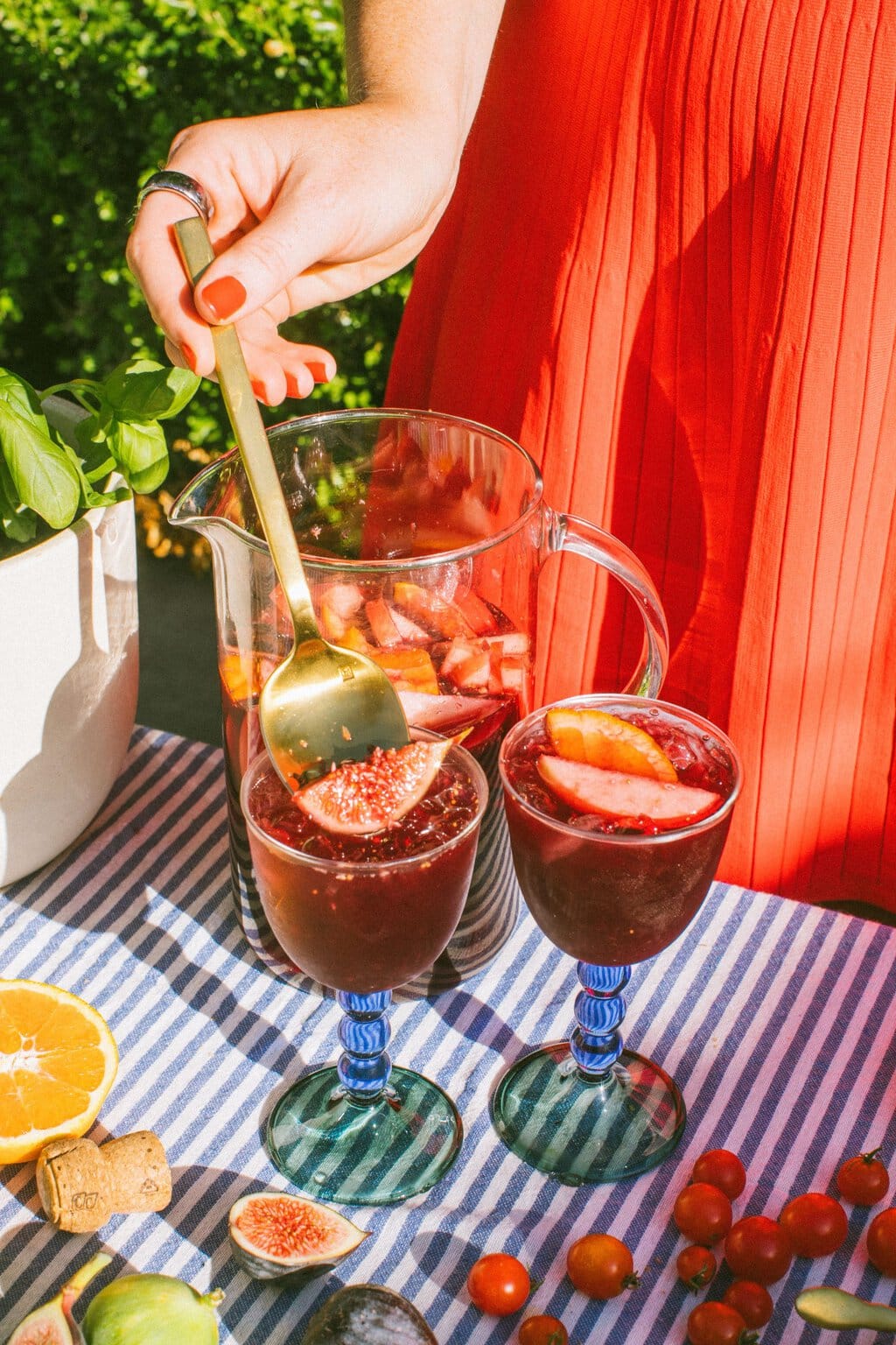 a large pitcher of sangria with two full glasses in front garnished with sliced fruit and a golden spoon stirring one