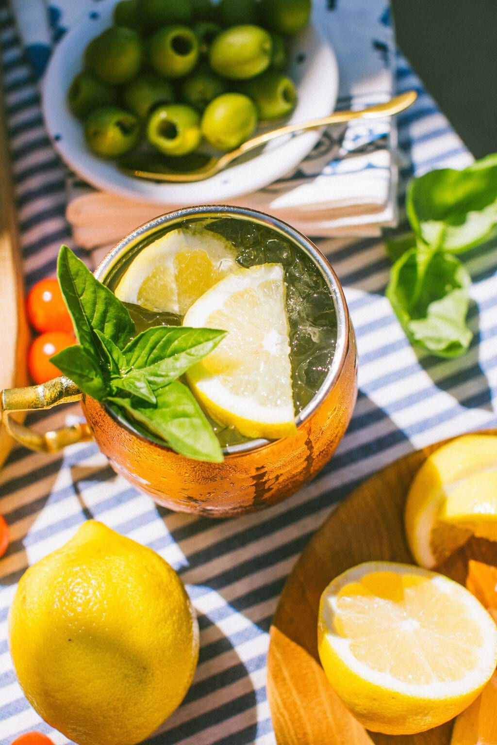 an overhead shot of a limoncello mule garnished with lemon wedges and mint leaves on a blue and white striped table cloth