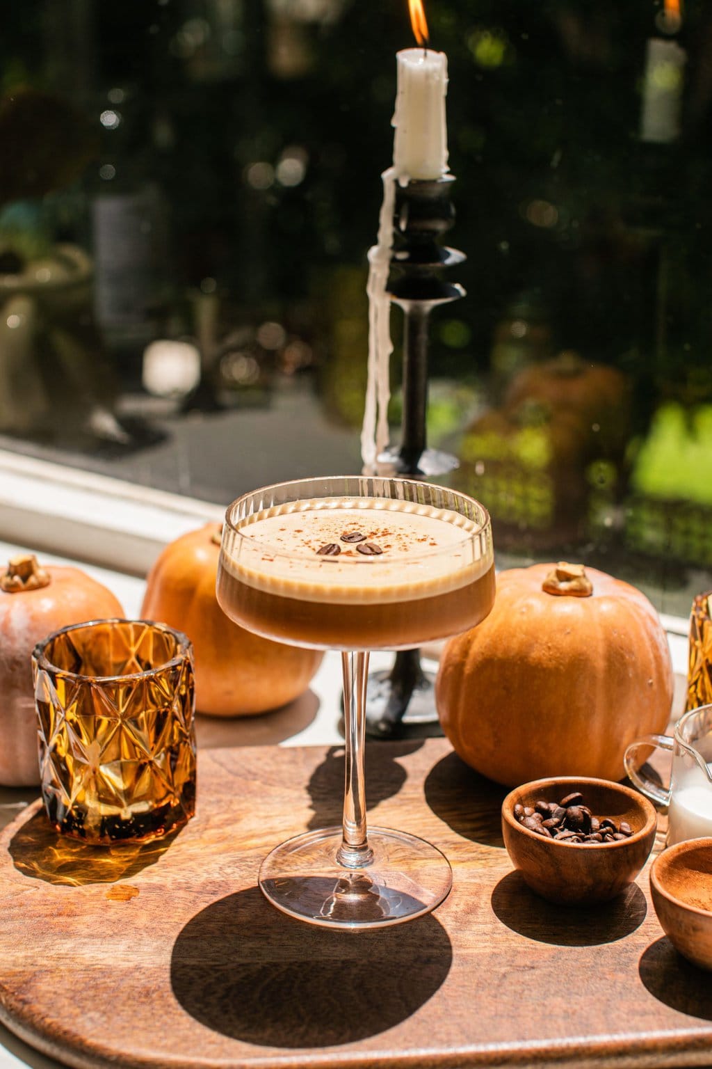 a single espresso martini with pumpkin spice and small pumpkins in the background as decor